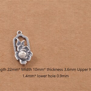 May include: Silver charm featuring a detailed floral design with a flower and leaves. The charm is 22 mm long, 10 mm wide, and 3.6 mm thick. It has two holes, one 1.4 mm and the other 0.9 mm.