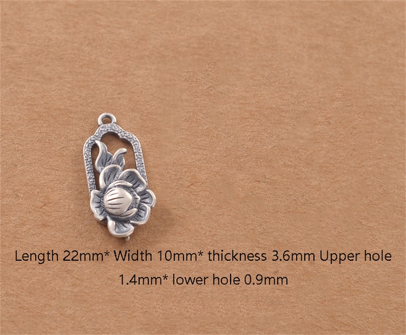 May include: Silver charm featuring a detailed floral design with a flower and leaves. The charm is 22 mm long, 10 mm wide, and 3.6 mm thick. It has two holes, one 1.4 mm and the other 0.9 mm.