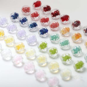 May include: A collection of colorful, round beads with a textured, clear outer layer. The beads are filled with various colors, including red, blue, green, yellow, and pink. The beads are arranged on a white surface.