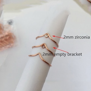 Puede incluir: Tres anillos de color dorado, dos con un soporte vacío de 2 mm y uno con una piedra de circonita de 2 mm.