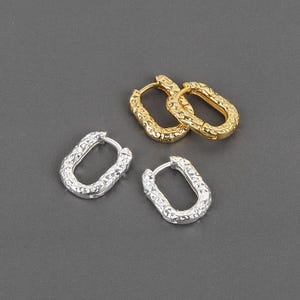 Puede incluir: Dos pares de pendientes de aro ovalados plateados y un par de pendientes de aro ovalados dorados. Los pendientes tienen un aspecto metálico texturizado y martillado. Los pendientes se muestran sobre una superficie gris.