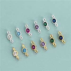 May include: Assortment of 10 silver and gold colored connector charms with different colored gemstones. Each charm features a double loop design and a single round gemstone in the center.