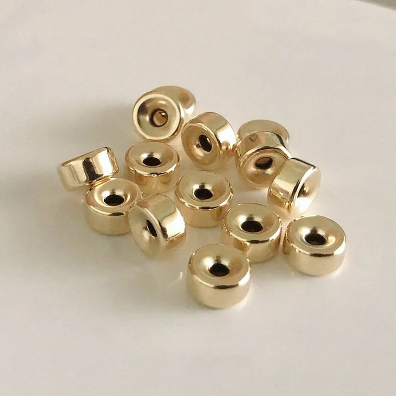 May include: A group of 14 gold-colored metal beads with a hole in the center. The beads are round and have a slightly raised edge.