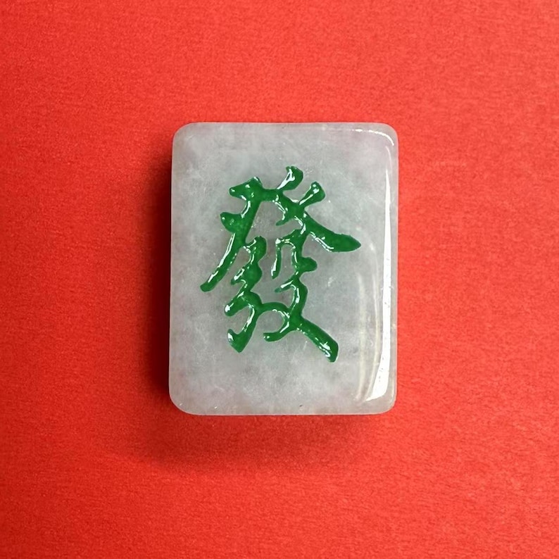 May include: A white mahjong tile with a green Chinese character on it. The character is "發" which means "prosperity" in English.