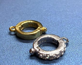 May include: Two jewellery clasps, one gold and one silver. The silver clasp has a row of small clear stones around the edge.