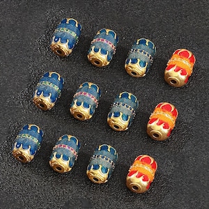 Puede incluir: Una colección de cuentas decorativas en varios colores. Las cuentas son cilíndricas con detalles dorados y presentan diseños de esmalte azul, rojo y naranja. Algunas cuentas tienen adornos de piedras preciosas.