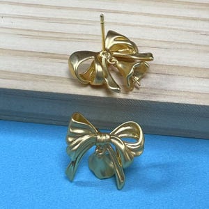 Könnte beinhalten: Ein Paar goldfarbene Schleifenohrringe. Die Ohrringe sind aus Metall und haben eine Schleifenform. Die Schleifen haben einen Durchmesser von etwa 2,5 cm.