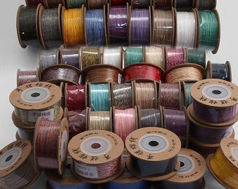 May include: A collection of numerous spools of 1.0mm cord in a wide variety of solid colors and multi-colored patterns. Each spool features a circular cardboard end cap with printed Chinese characters and the text 1.0mm, arranged in a stacked display.