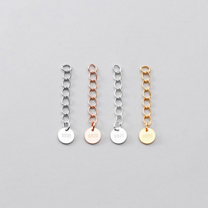 May include: Four silver chain extenders with a round tag at the end. Each tag is stamped with "S925" and the chains are silver, rose gold, gold, and silver.