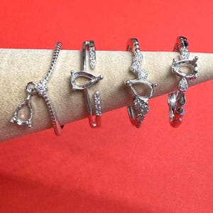 May include: Four silver rings with pear-shaped settings and small clear stones. The rings are on a white display stand.