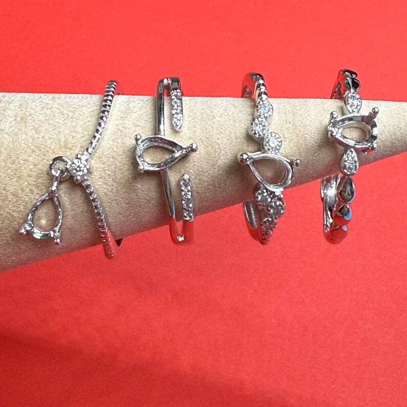 May include: Four silver rings with pear-shaped settings and small clear stones. The rings are on a white display stand.
