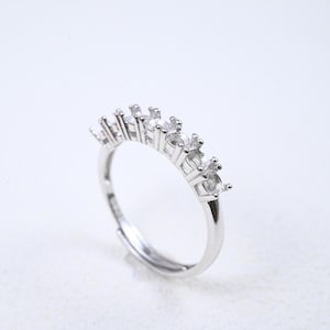 May include: A silver ring featuring a line of clear, sparkling stones. The ring has an adjustable band. The stones are evenly spaced and set against a white backdrop. The ring is a piece of jewellery.