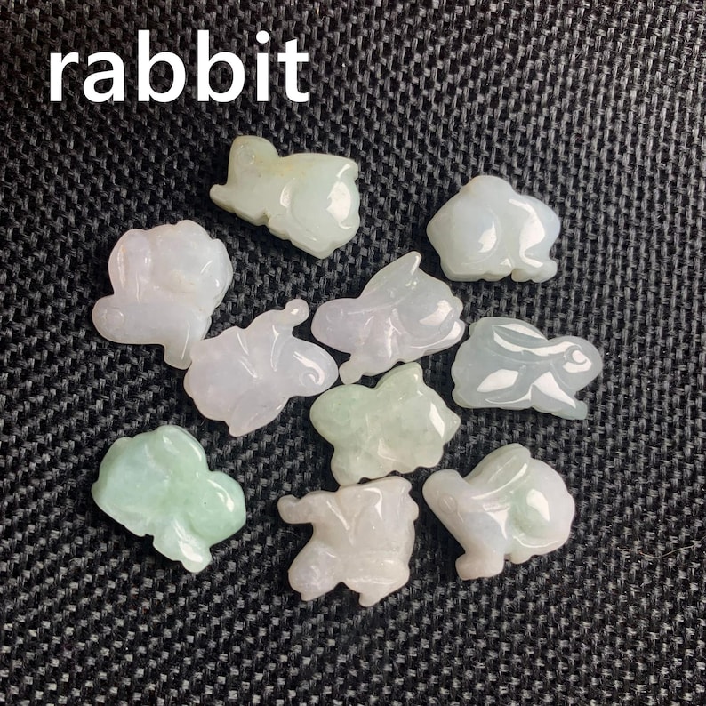 Pode incluir: Uma cole&ccedil;&atilde;o de pequenas figuras de coelho esculpidas em jade, em tons de branco e verde. A palavra "rabbit" est&aacute; escrita em texto branco no topo. As figuras s&atilde;o exibidas em uma superf&iacute;cie escura e texturizada.