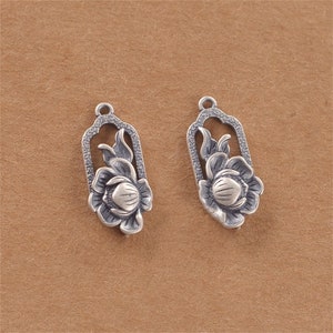 May include: Two silver-toned flower charm pendants with intricate details. Each pendant features a stylised flower with a raised centre and delicate leaves.