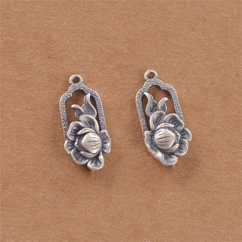 May include: Two silver-toned flower charm pendants with intricate details. Each pendant features a stylised flower with a raised centre and delicate leaves.