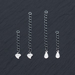 May include: Four silver chain extenders with different charms. The charms are a heart, a teardrop, and two more hearts. Each charm is stamped with "S925".