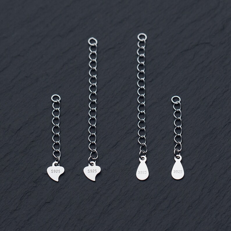 May include: Four silver chain extenders with different charms. The charms are a heart, a teardrop, and two more hearts. Each charm is stamped with "S925".