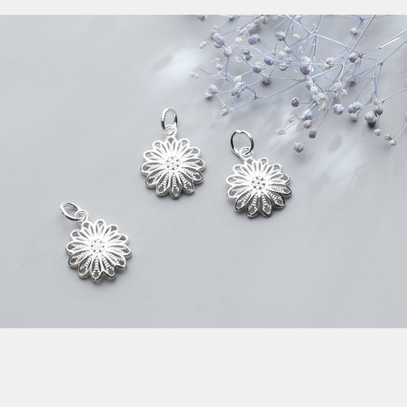 May include: Three silver filigree flower charms with a delicate, intricate design. The charms are perfect for adding a touch of elegance to jewelry projects.