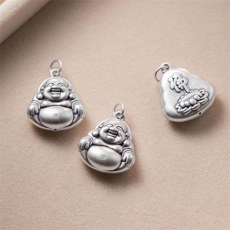 Pu&ograve; includere: Tre ciondoli d'argento con un Buddha sorridente, un Buddha sorridente e un ciondolo a forma di cuore con caratteri cinesi e un fiore di loto.
