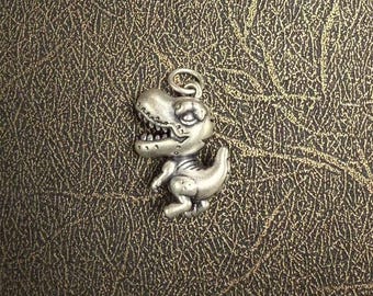 May include: Silver charm in the shape of a dinosaur. The dinosaur is standing on its hind legs with its mouth open. The charm is detailed and has a realistic look.