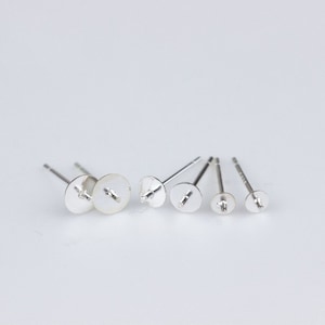 May include: Five silver earring posts with round, flat backs. The posts are different sizes.