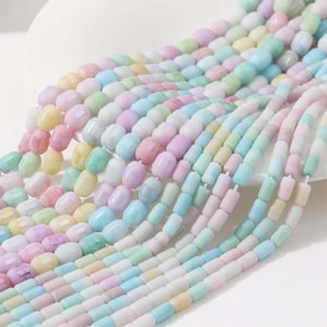 May include: Strands of pastel-colored beads in shades of pink, yellow, blue, and green. The beads are cylindrical with rounded edges, strung together to create a flowing, textured appearance. The beads are arranged in a layered pattern.