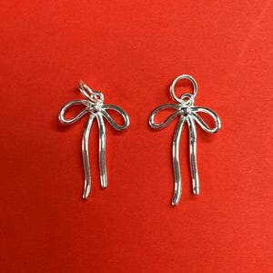 May include: Two silver bow charms with a loop at the top for attaching to a necklace or bracelet. The bows are detailed with a small bead at the centre.