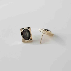 May include: A pair of gold-toned earrings with oval-shaped black stones set in square frames.