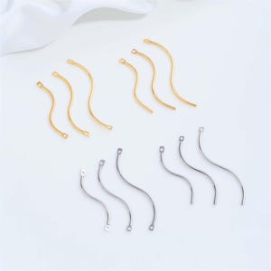 May include: A collection of twelve metal jewelry components shaped like elongated, gentle S-curves. Six of the pieces are gold-toned and six are silver-toned. Each curved bar features a small circular loop at both ends for attachment purposes.