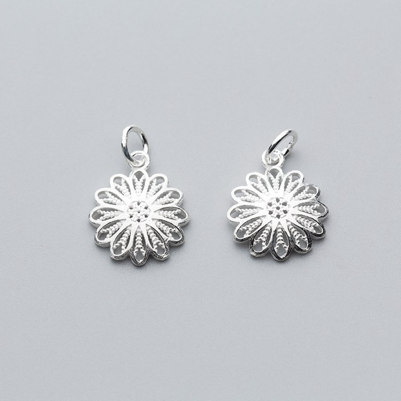 May include: Two silver filigree flower charms with a delicate, intricate design. The charms are perfect for adding a touch of elegance to jewelry projects.