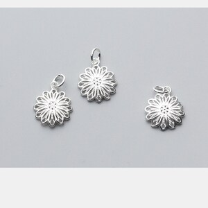 May include: Three silver filigree flower charms with a loop for attaching to a necklace or bracelet.
