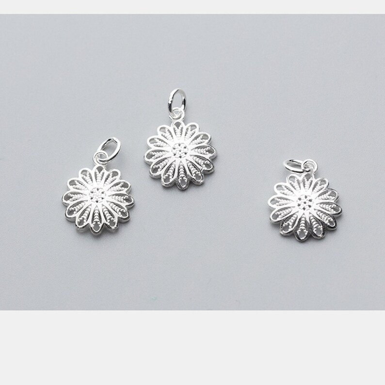 May include: Three silver filigree flower charms with a loop for attaching to a necklace or bracelet.