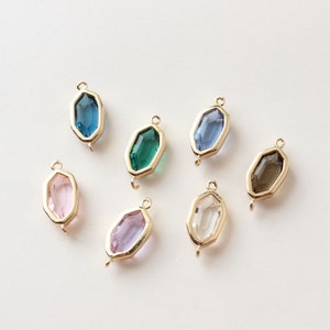 May include: Seven gemstone pendants in various colors, including blue, green, pink, purple, and clear. Each pendant has a gold-colored frame and a small loop for attaching to a chain or other jewelry component.