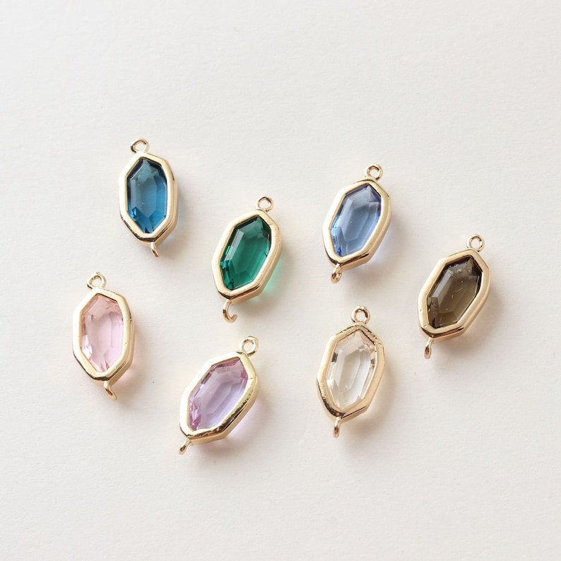 May include: Seven gemstone pendants in various colors, including blue, green, pink, purple, and clear. Each pendant has a gold-colored frame and a small loop for attaching to a chain or other jewelry component.