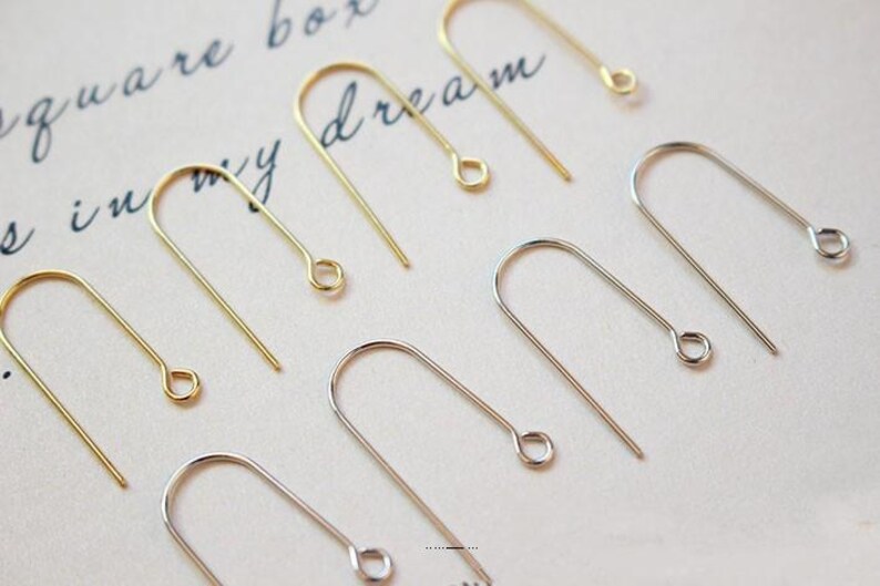 May include: A close-up of a set of gold and silver earring hooks. The hooks are made of metal and have a simple design.
