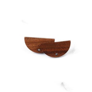 Pode incluir: Dois brincos de madeira semicirculares com acabamento castanho escuro. Cada brinco tem um pequeno orifício perto da borda plana. Os brincos são exibidos em um fundo branco.