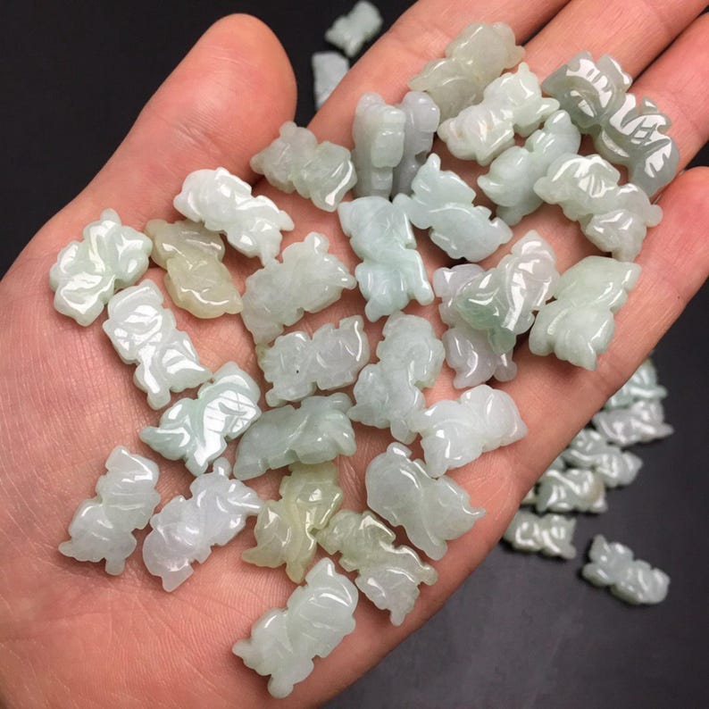 Pode incluir: Uma cole&ccedil;&atilde;o de pequenas figuras de animais em jade. Cada figura &eacute; esculpida com detalhes intrincados, exibindo tons de verde e branco. As figuras s&atilde;o seguradas em uma m&atilde;o, com um fundo escuro que destaca os detalhes.