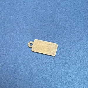 Op de afbeelding: Een klein, leeg, goudkleurig metalen label met een gat bovenaan om een ​​touwtje of lint aan te bevestigen.