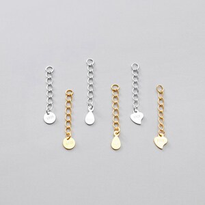 May include: Six silver and gold chain extenders with different charms. The charms include a circle, a teardrop, and a heart. The chains are all about 2 inches long.