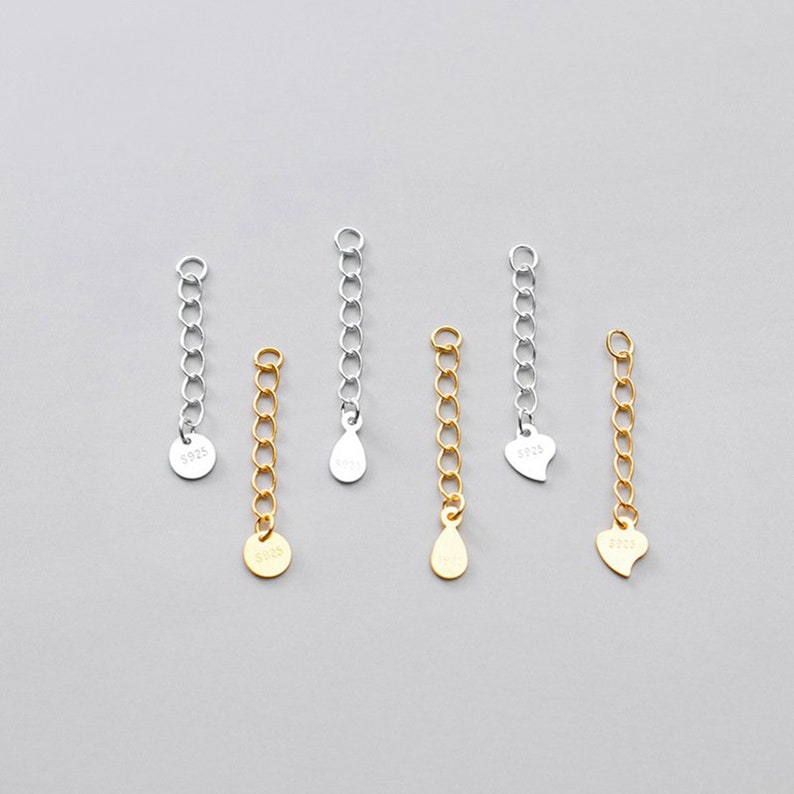 May include: Six silver and gold chain extenders with different charms. The charms include a circle, a teardrop, and a heart. The chains are all about 2 inches long.
