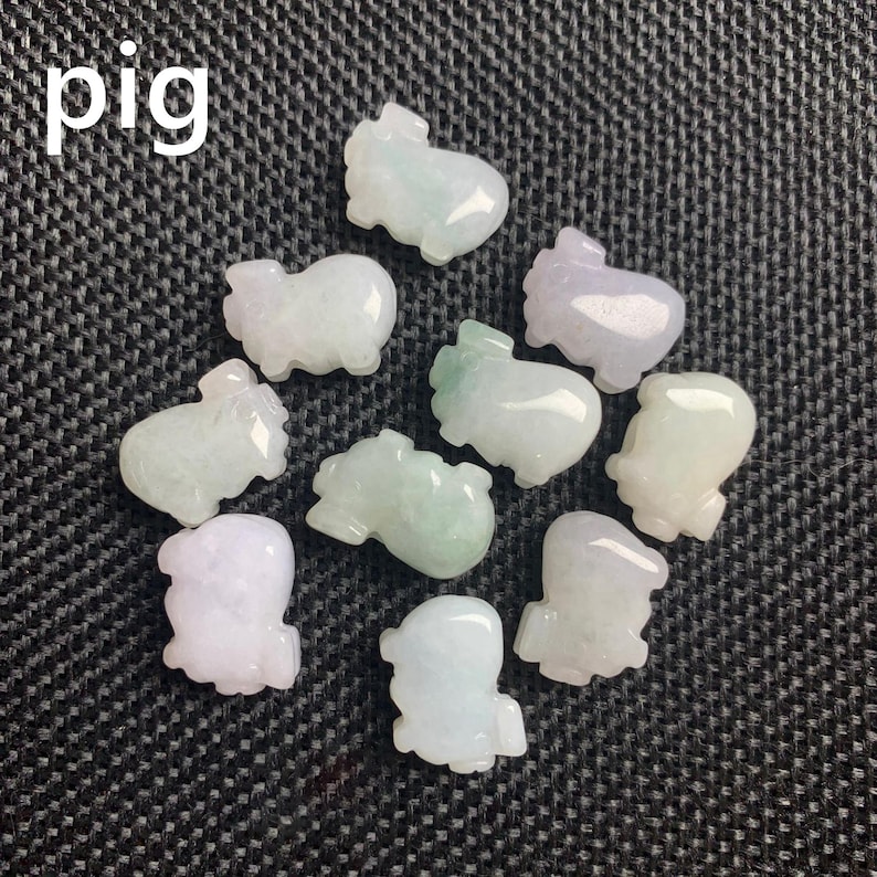 Pode incluir: Uma cole&ccedil;&atilde;o de pequenas figuras de porcos esculpidas em tons de verde, branco e lavanda. A palavra "pig" est&aacute; escrita em branco no canto superior esquerdo. As figuras est&atilde;o dispostas sobre uma superf&iacute;cie texturizada cinza escuro.