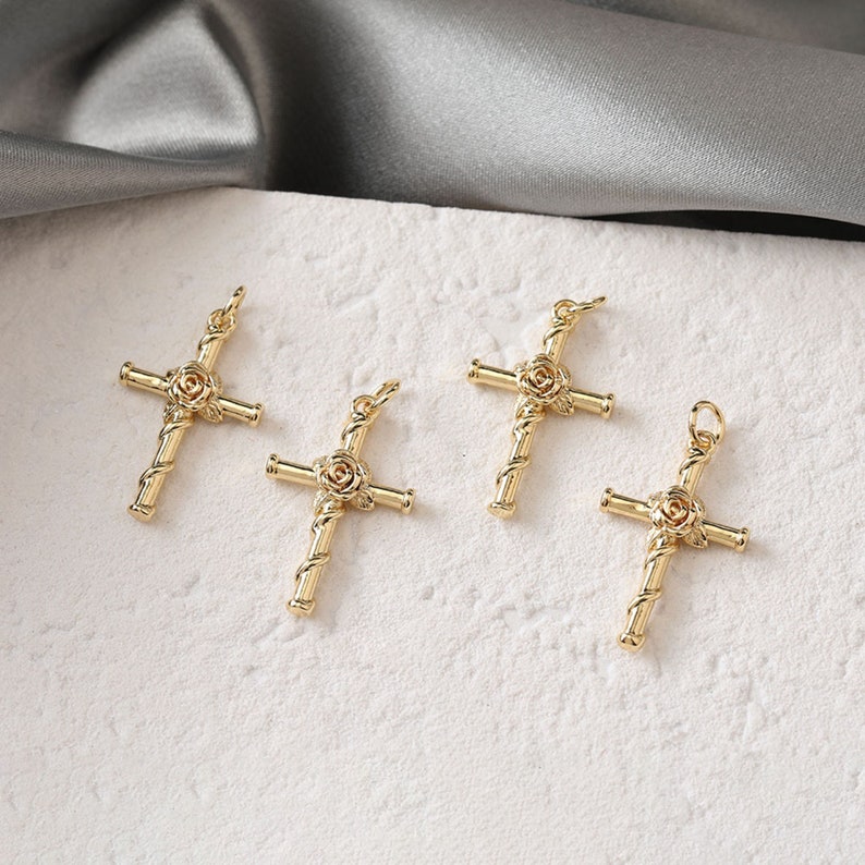 May include: Four gold-tone cross charms with a rose design. The crosses are made of twisted metal and have a rose in the center.