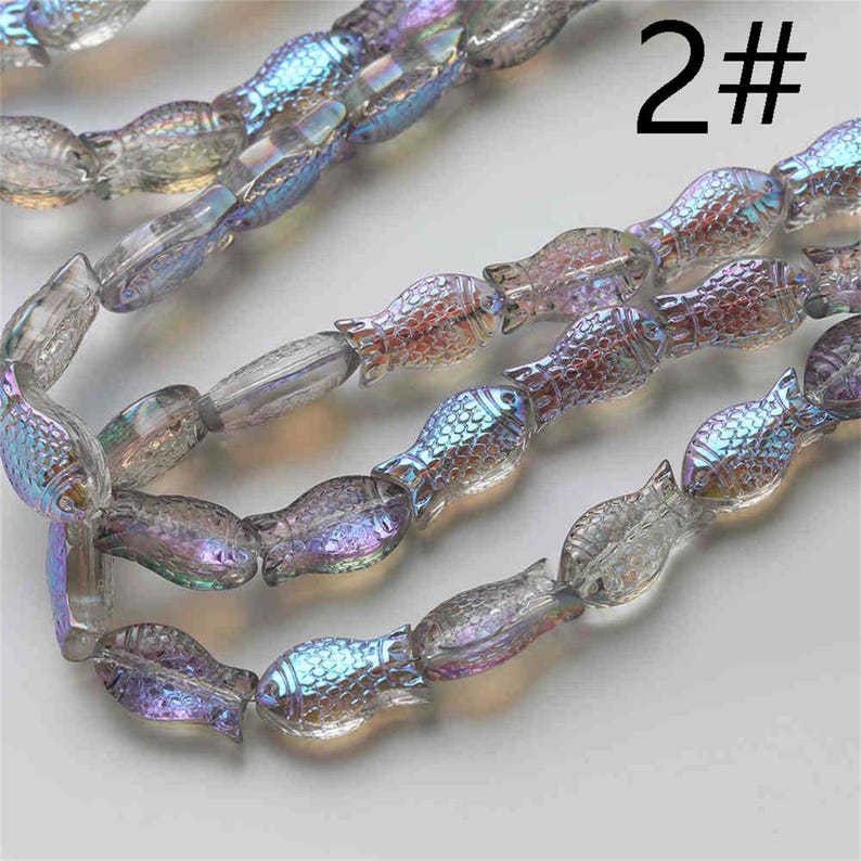 May include: A strand of iridescent glass fish beads. The beads are translucent and have a rainbow sheen. The beads are strung on a clear thread. The image includes the text "2#"