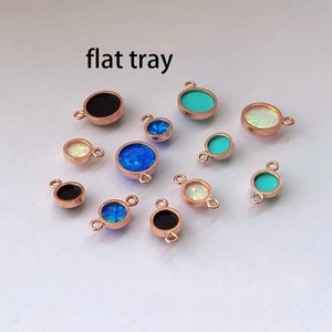 May include: A flat tray of assorted round charms with different colored stones. The charms are made of rose gold metal and have a loop on the top for attaching to jewelry. The stones are black, white, blue, and turquoise.
