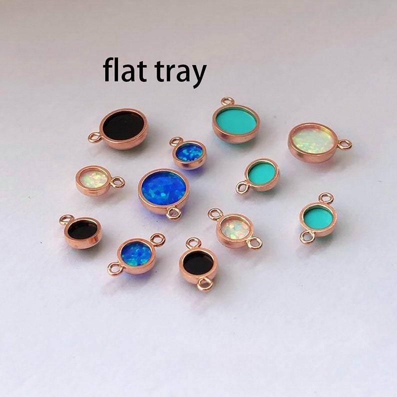 May include: A flat tray of assorted round charms with different colored stones. The charms are made of rose gold metal and have a loop on the top for attaching to jewelry. The stones are black, white, blue, and turquoise.