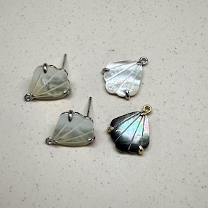 May include: Four shell-shaped earring findings, two with silver posts and two with gold jump rings. Two are white with a pearlescent finish and two are black with an iridescent finish.