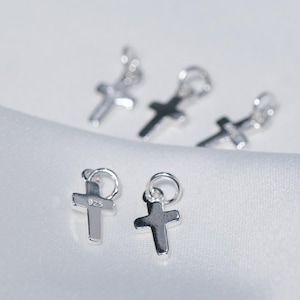 Può includere: Diversi piccoli ciondoli a forma di croce color argento con anelli per la creazione di gioielli. Le croci sono esposte su una superficie bianca leggermente strutturata. Un ciondolo è timbrato con "925".