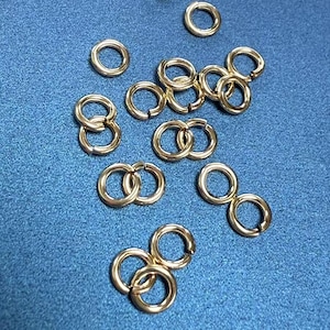 May include: A group of gold jump rings, some are linked together, on a blue background.