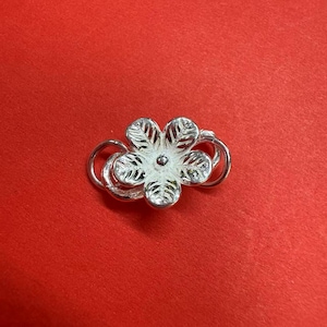 May include: Silver flower charm with a detailed design. The charm is made of metal and has a shiny finish.