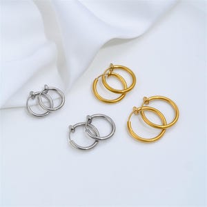 Peut inclure: Trois paires de boucles d'oreilles créoles au design circulaire. Une paire est argentée et deux paires sont dorées. Chaque boucle d'oreille dispose d'un mécanisme à clip à ressort pour oreilles non percées, composé d'un anneau fin et d'un petit disque plat.